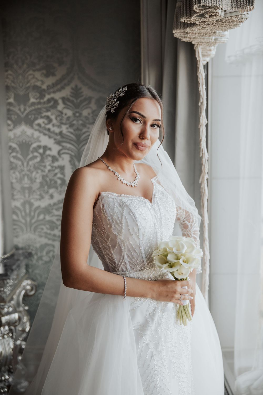 A bridal portrait in a luxurious room featuring an elegant white lace wedding gown and crystal chandelier.