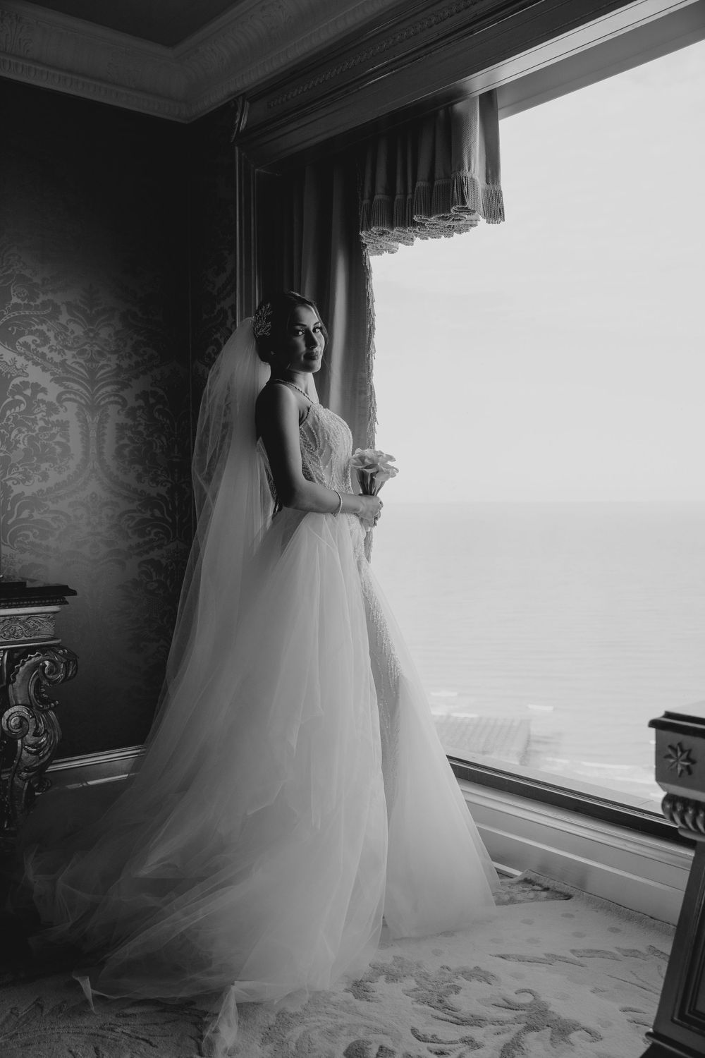 Dramatic black and white bridal portrait by a large window with city views.