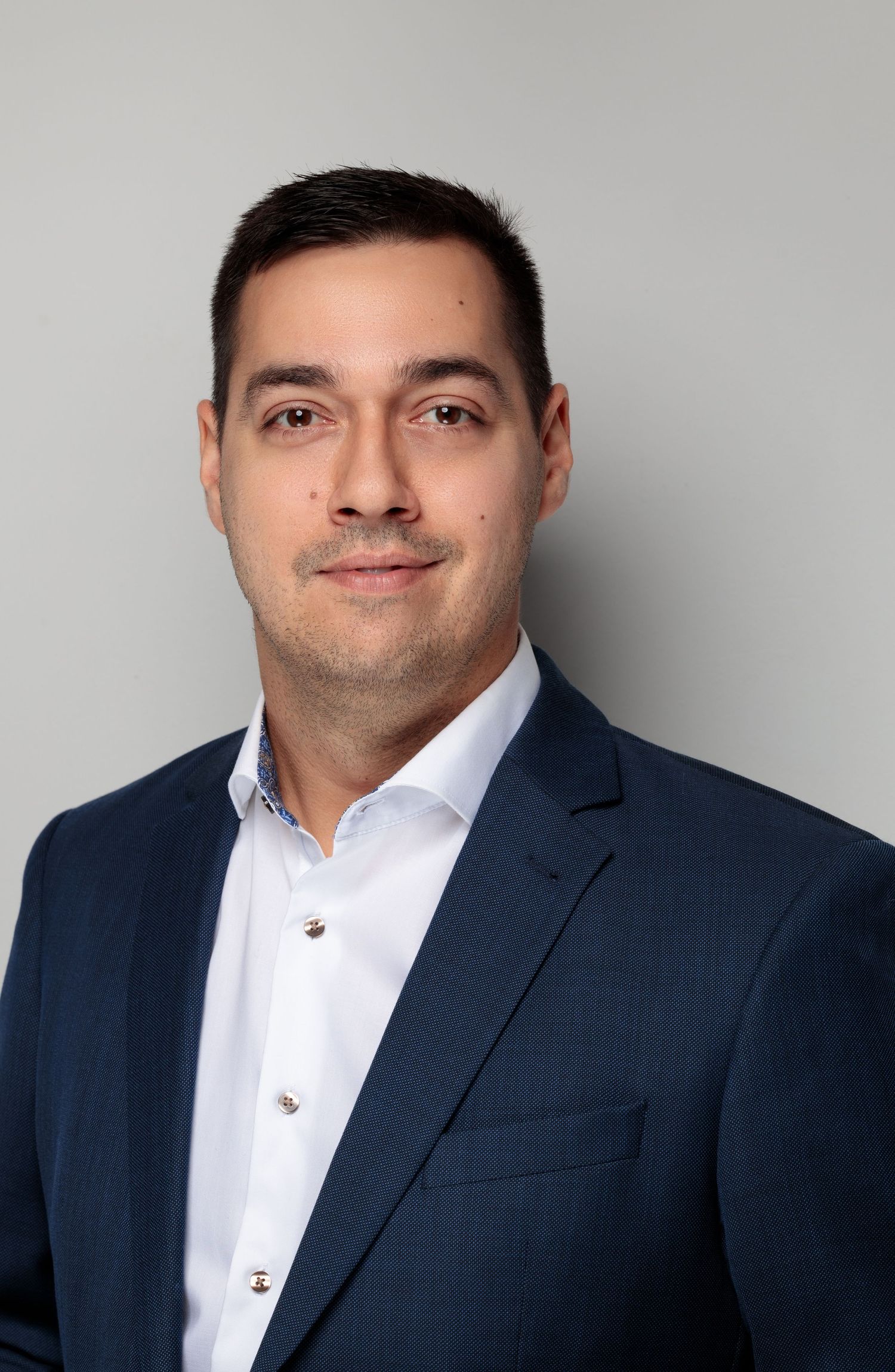Corporate headshot of professional in navy suit and white button-down shirt.