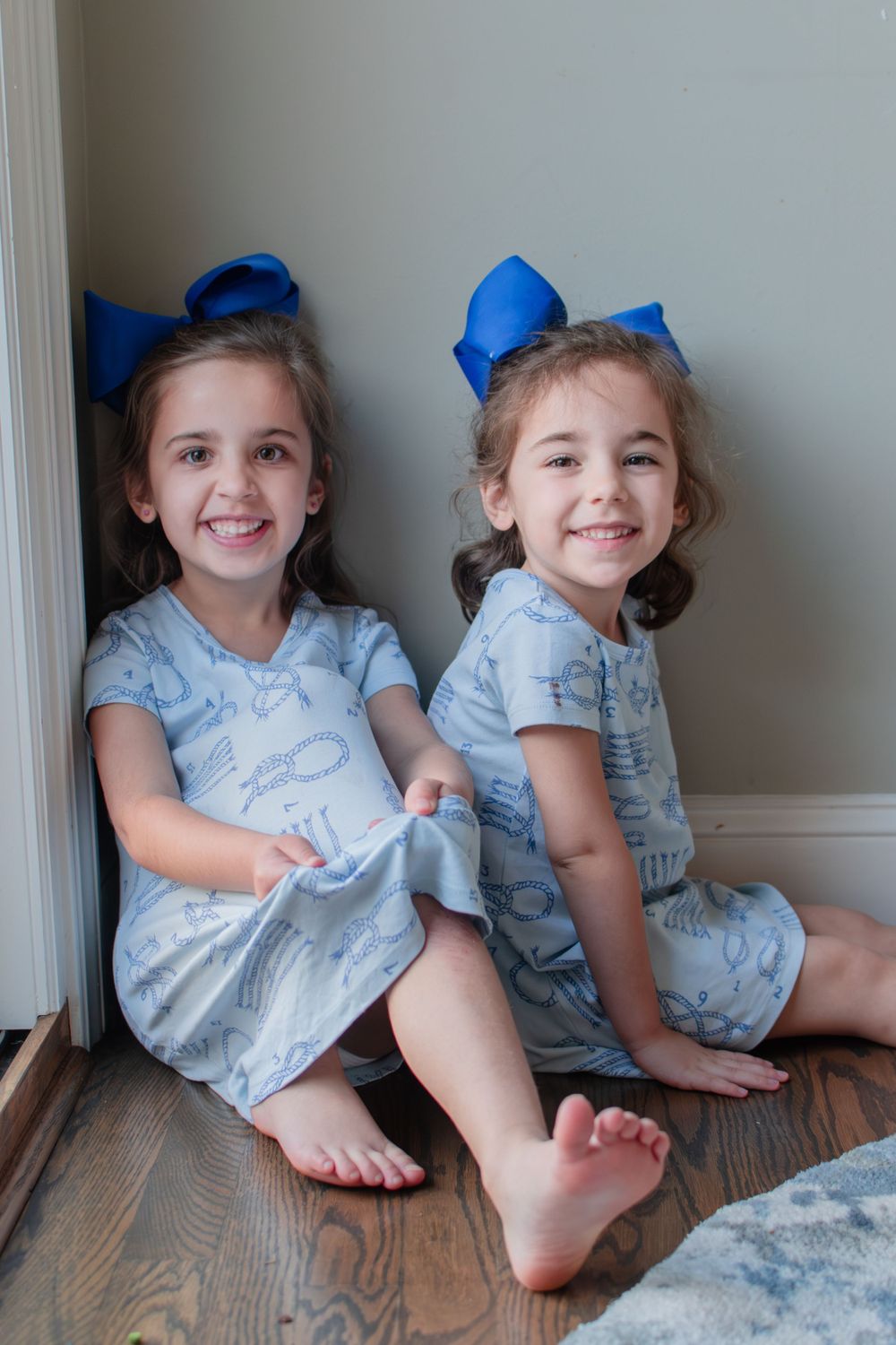 Two sisters look as they casually sit together in a corner of their home.