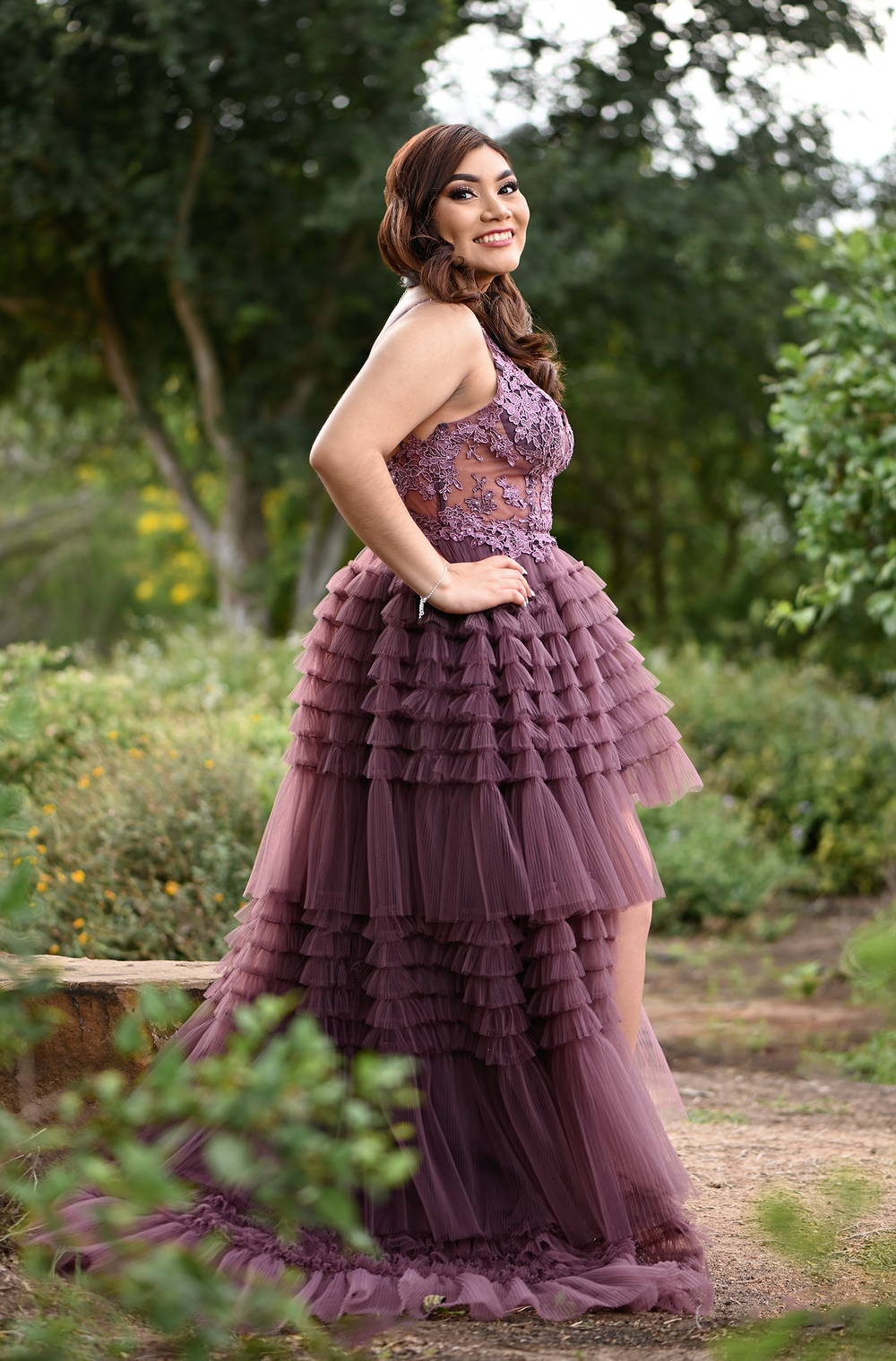 Full-length purple tulle gown with tiered ruffles and fitted lace bodice in outdoor garden setting.
