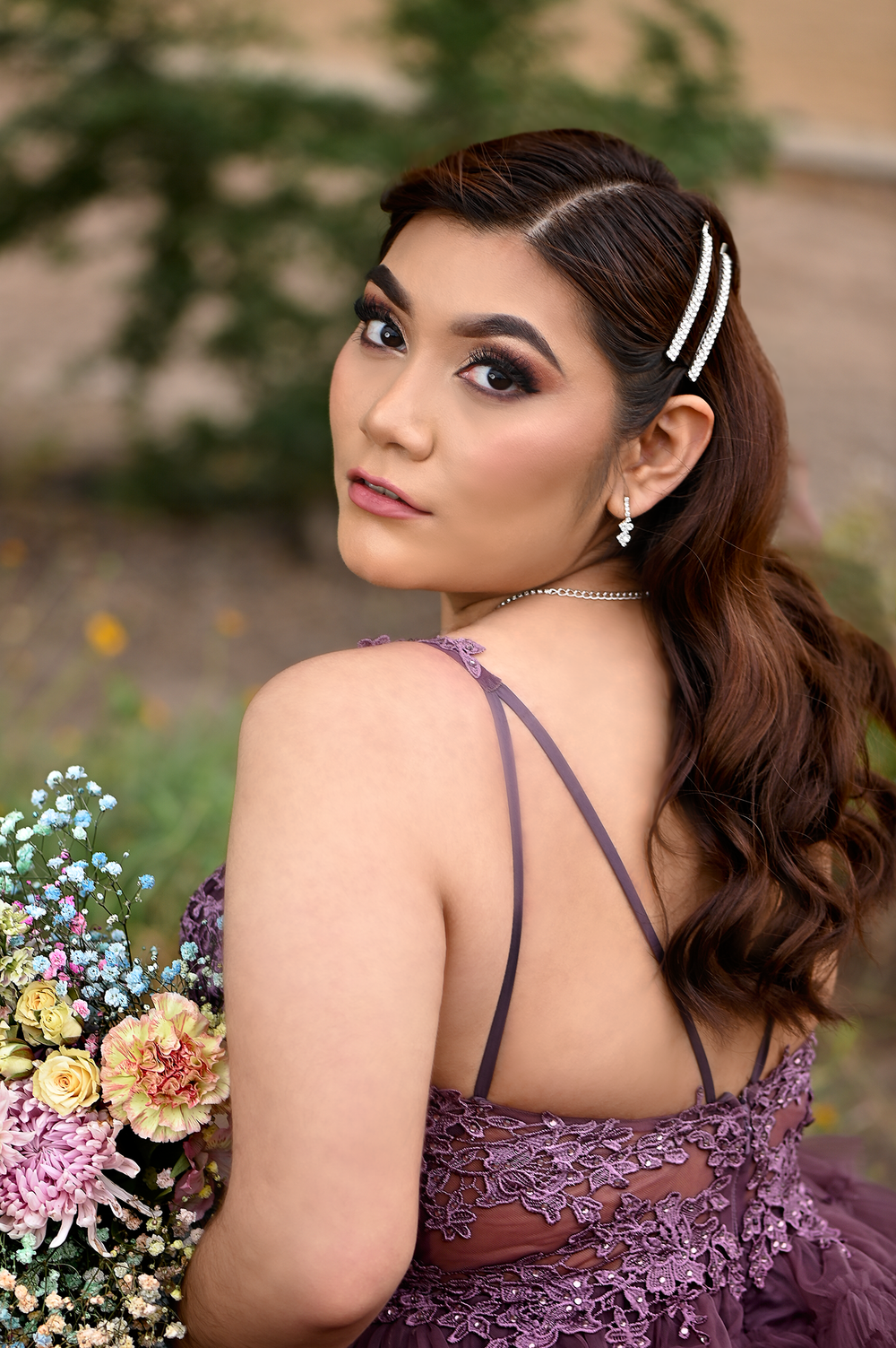Back detail of purple lace gown with crystal hair clips and colorful bouquet in garden setting.