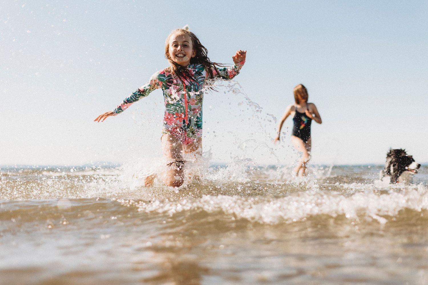 Children playing and splashing in ocean waves on a sunny summer day.