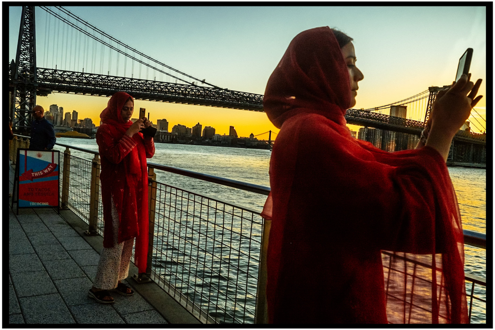 People in red coats taking photos at sunset near Manhattan Bridge. NYC street photography