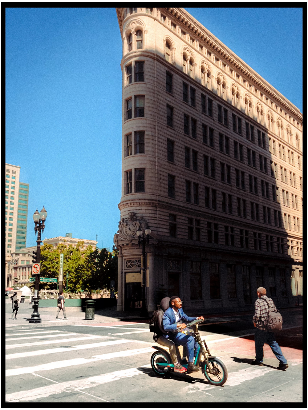 Historic Flatiron-style building on sunny street corner with cyclist passing by. Oakland streeet photography