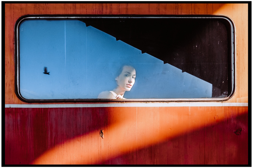 View through a red train window showing shadowy figure against blue sky. Portland street photography