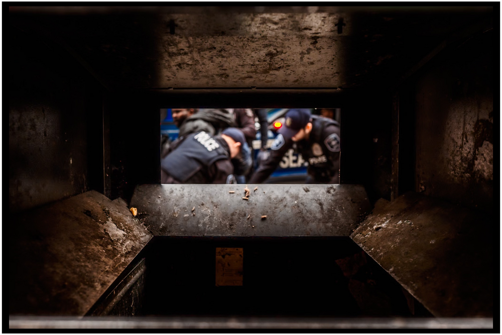 Dark framed view of a crowded scene through a rectangular window opening.