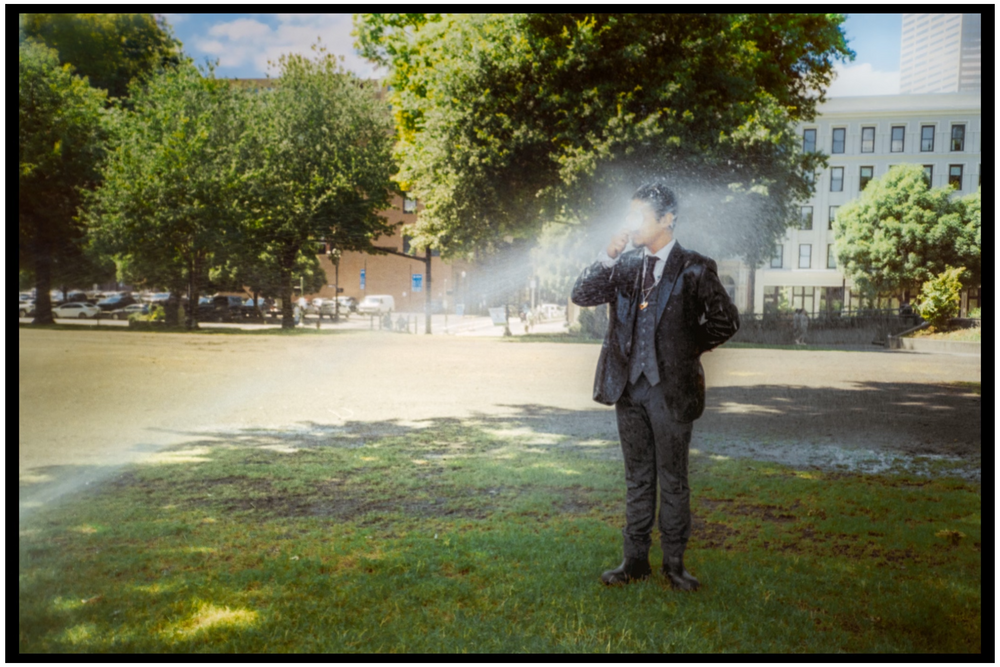 Figure standing in a misty park with sprinklers running on a sunny day. Portland street photography