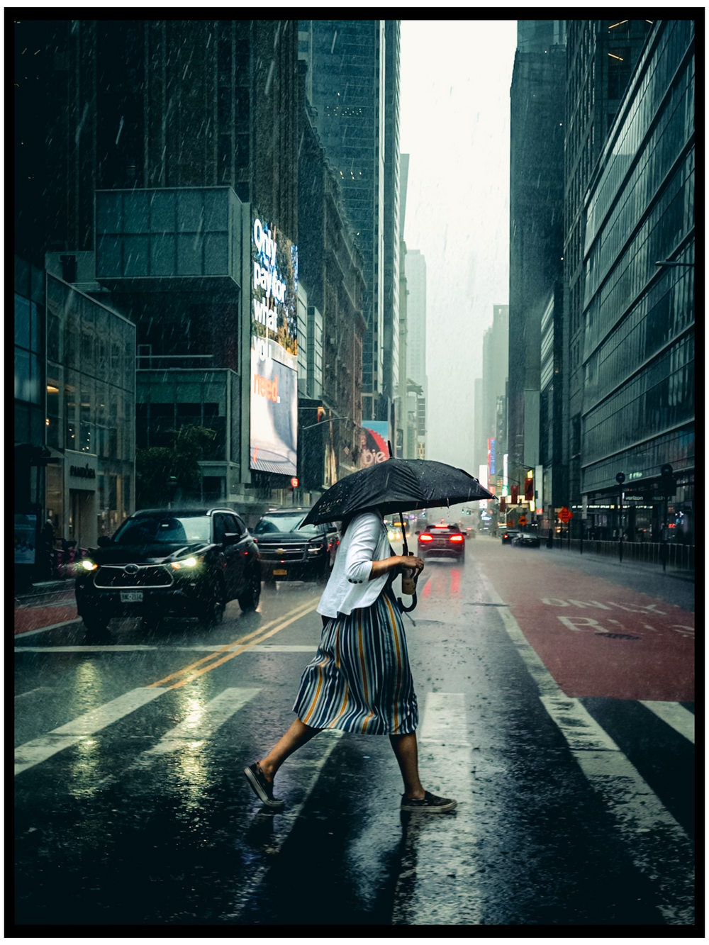 A figure with an umbrella crosses a rainy Manhattan street with towering buildings in the background. NYC street photography