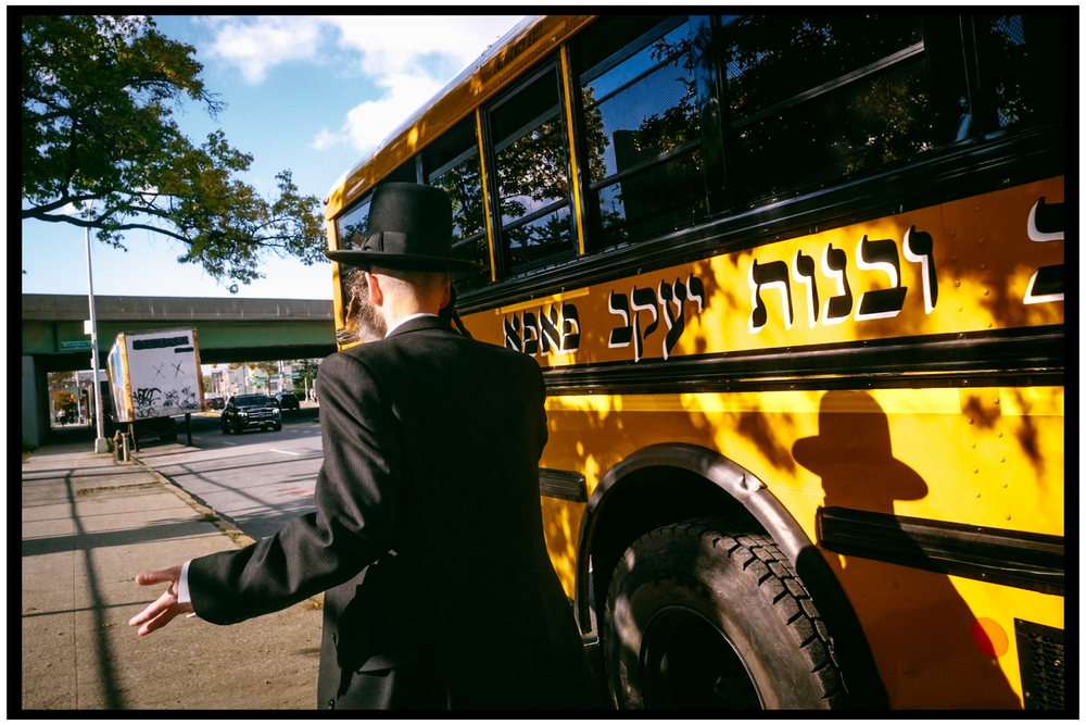 Yellow school bus with Hebrew lettering parked on street. NYC street photography