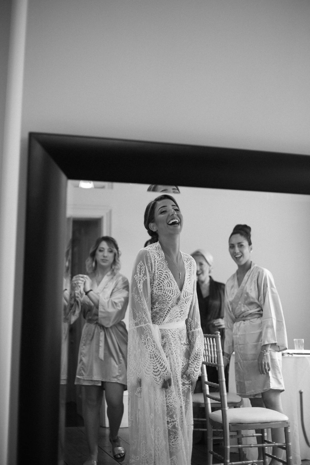 Black and white photo of bride getting ready with bridesmaids in matching robes.