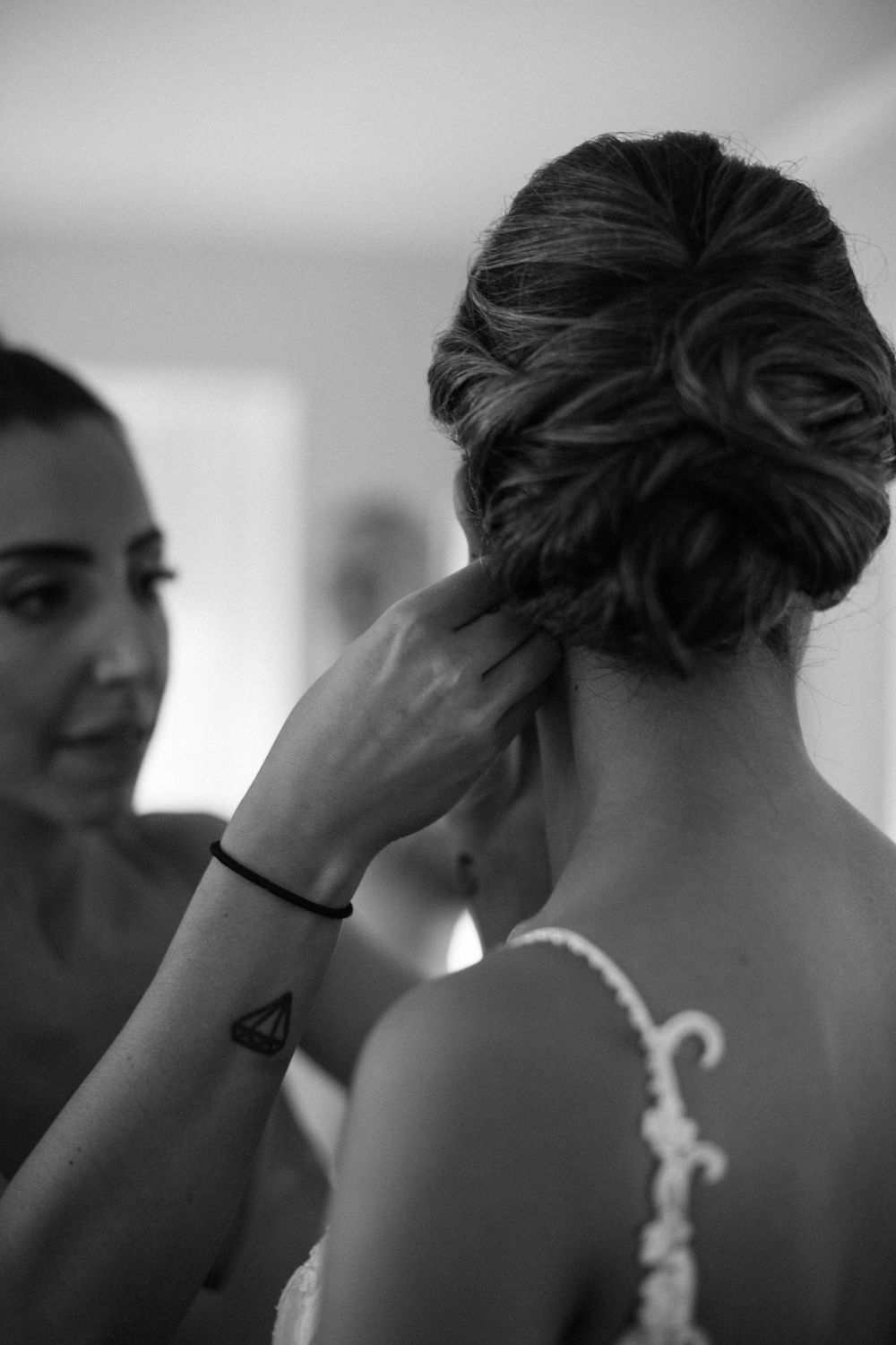 Stylist adjusts bride's elegant updo hairstyle in black and white photography.