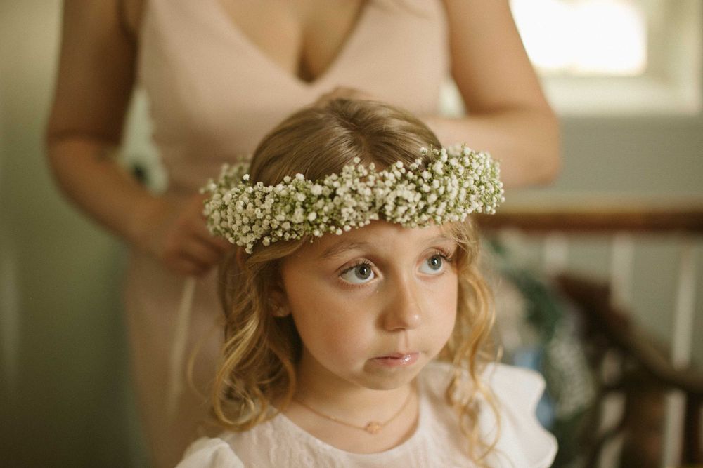 A young flower girl wearing a delicate baby's breath crown and white dress.