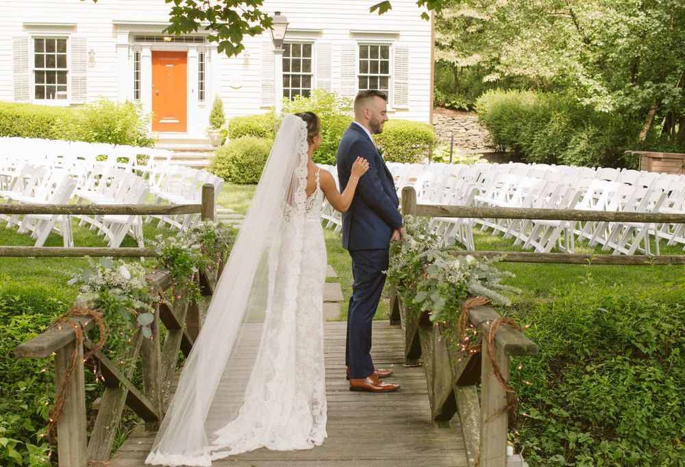 Romantic wedding couple sharing a moment on a rustic wooden bridge with white house in background.