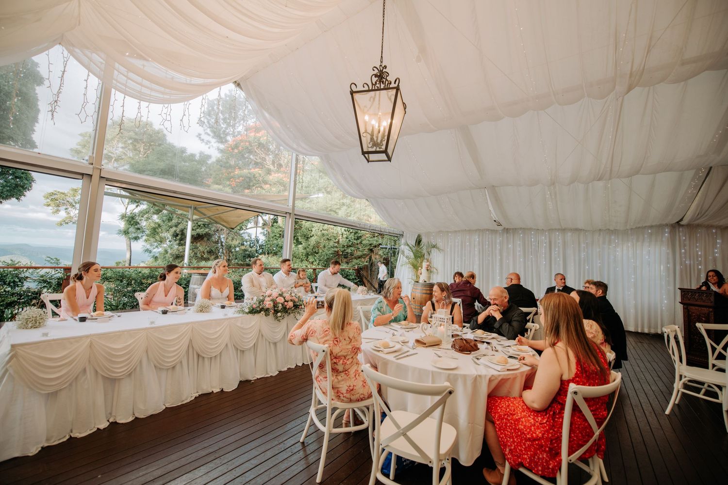 Wedding reception under white tent with guests seated at round tables.