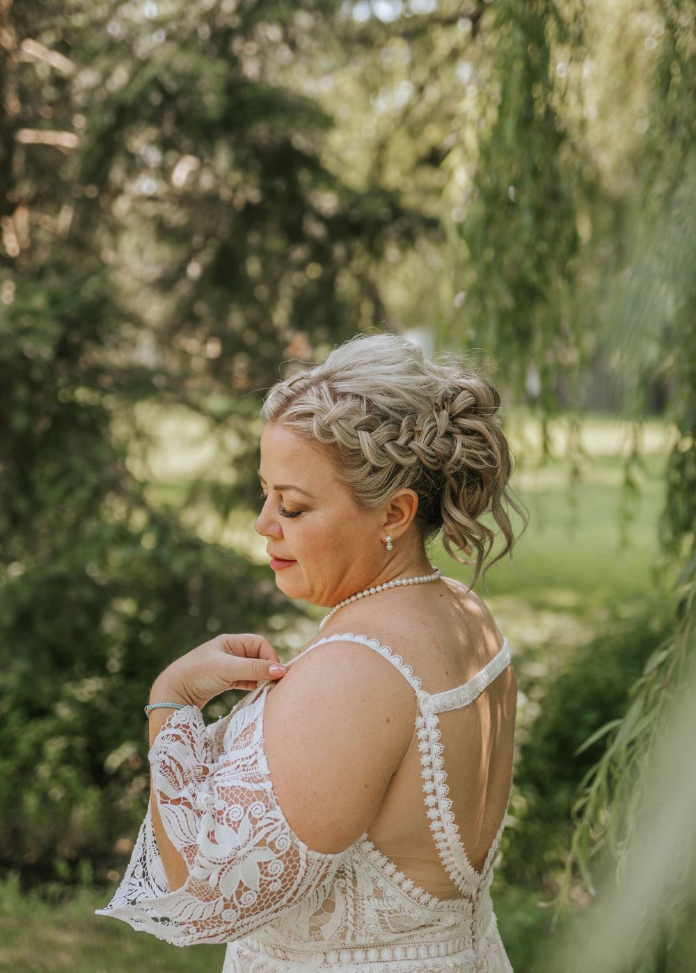 Close-up details of a lace wedding dress with pearl straps against a natural backdrop.