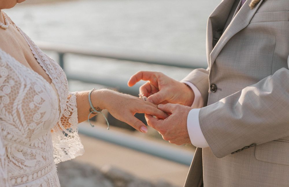 Close-up of wedding ring exchange ceremony with bride in lace dress and groom in gray suit.