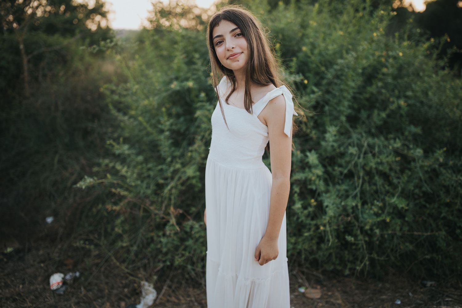 Outdoor portrait in white dress against green natural background at sunset.