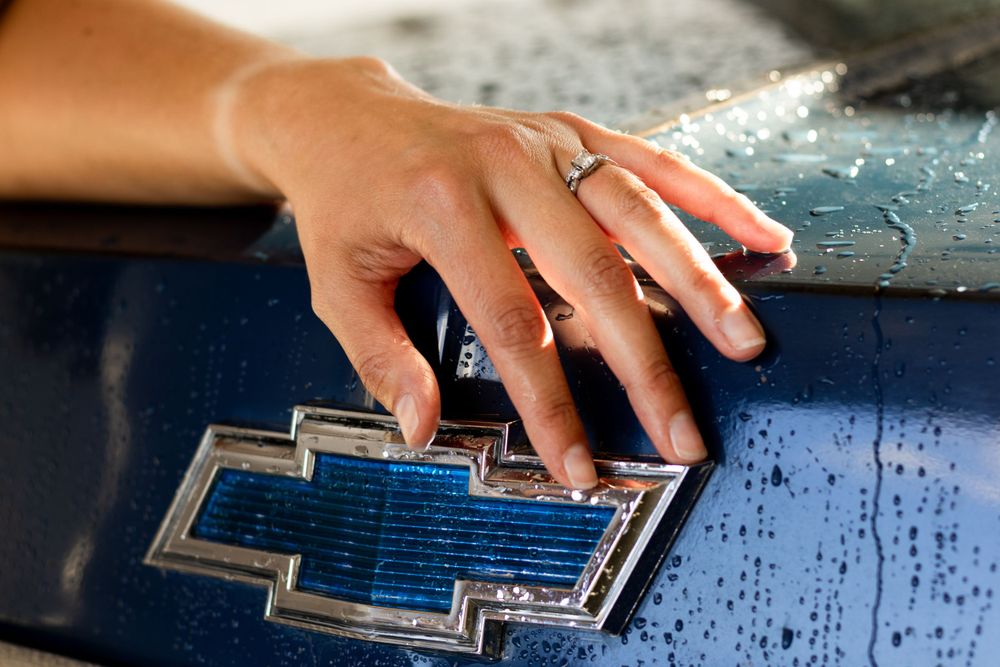 Close-up of a hand touching a blue Chevrolet emblem on a car.