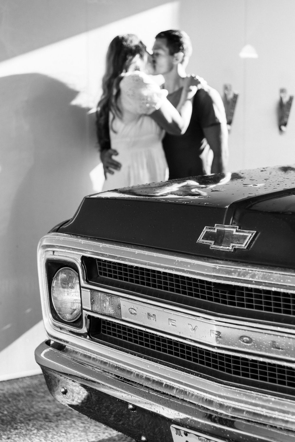 Romantic couple posing with classic Chevrolet truck in dramatic black and white lighting.