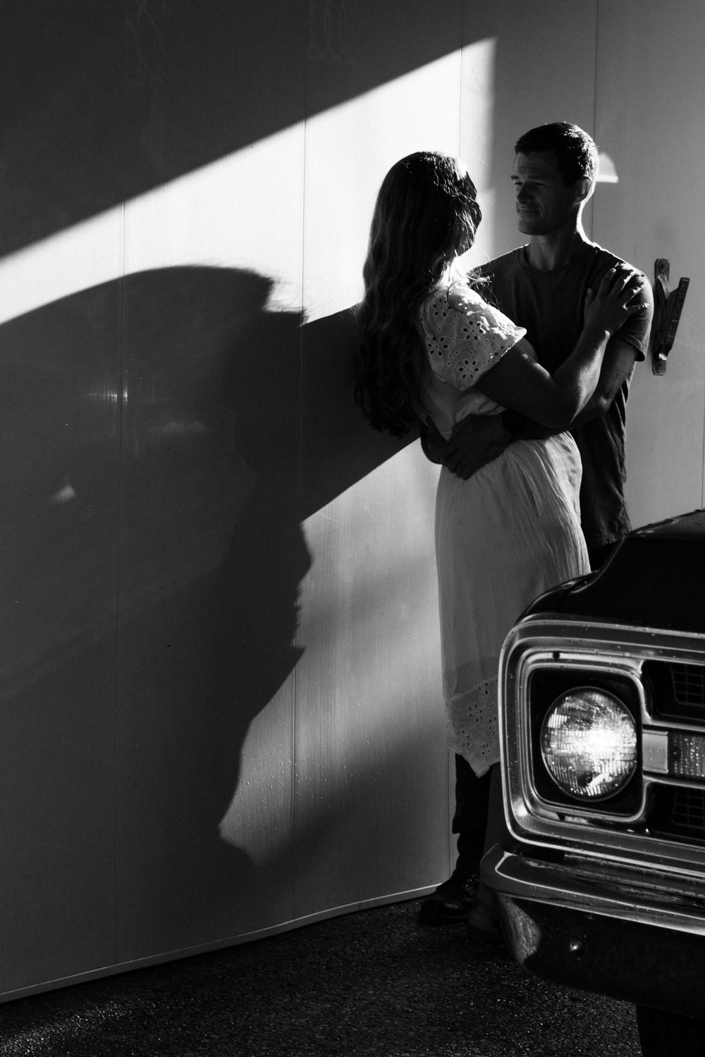 Silhouetted couple embracing against a wall next to a classic car headlight.