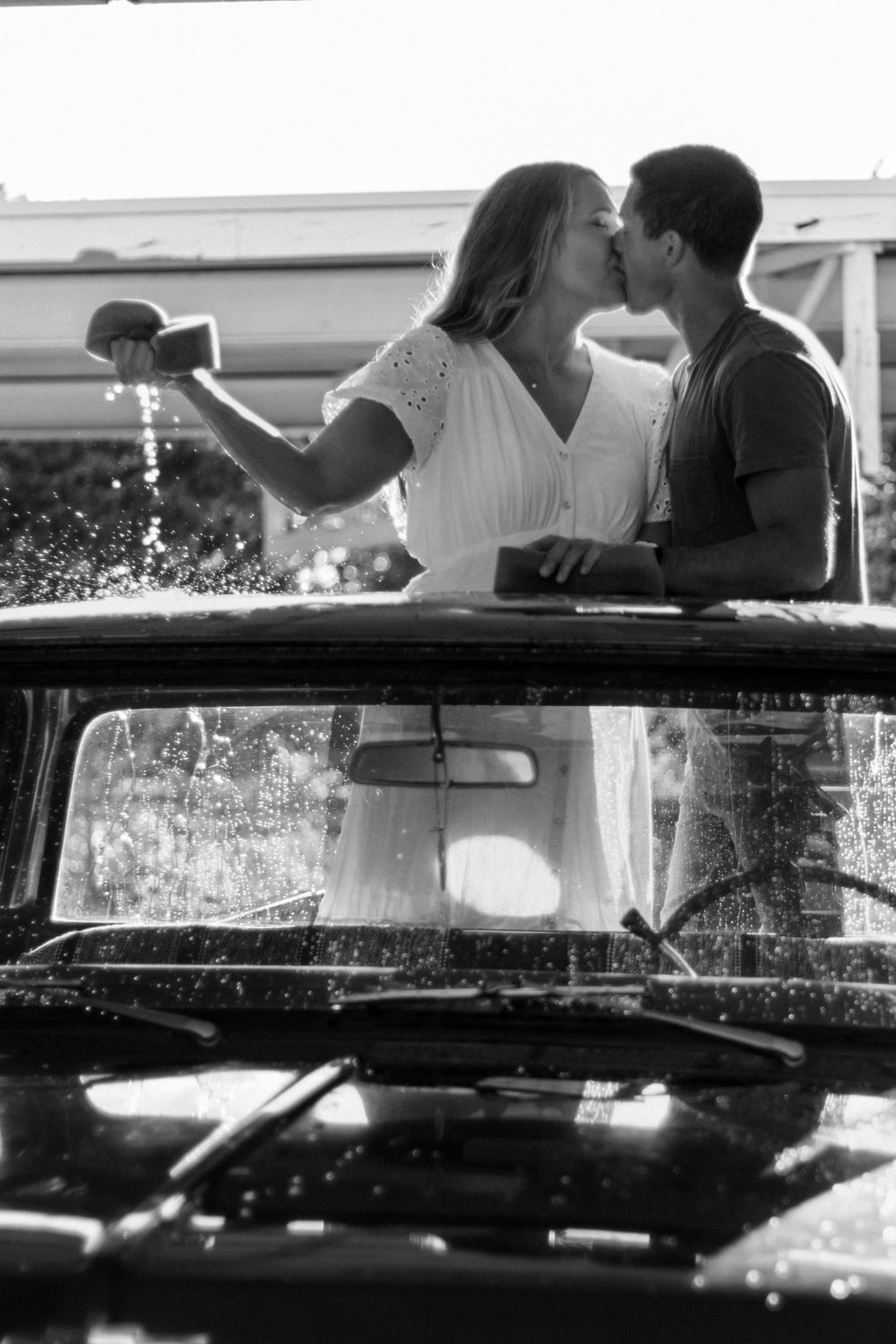 Couple sharing a tender moment while leaning on a classic car in monochrome.