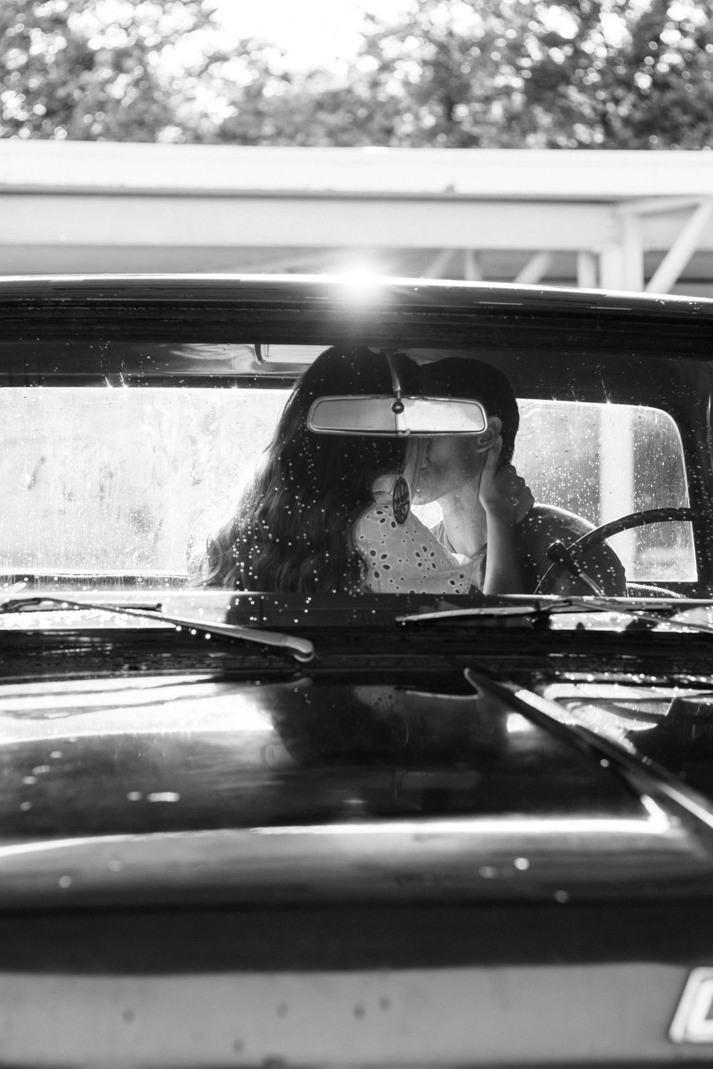 Romantic couple seen through a vintage car windshield in black and white photography.