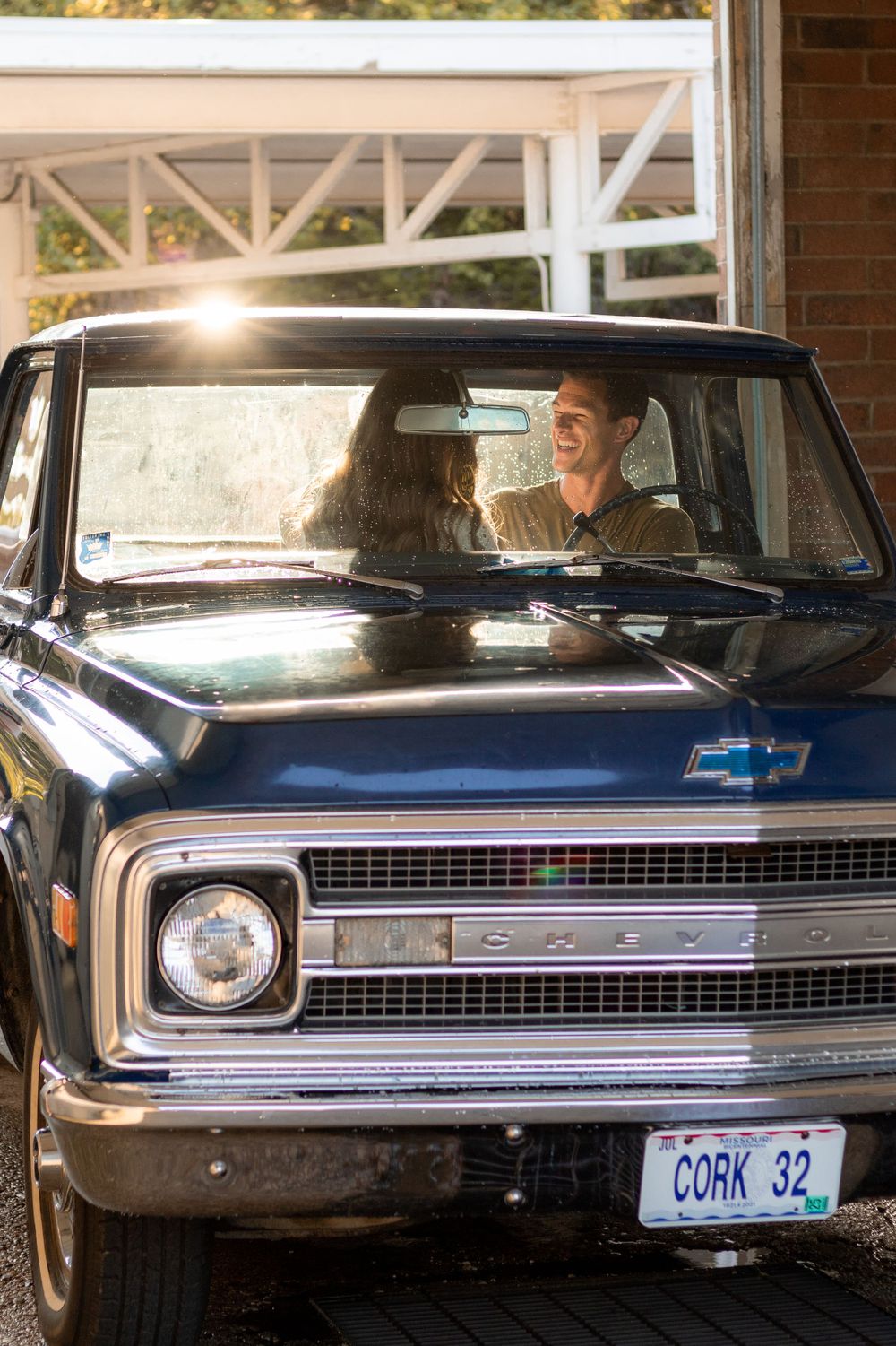 Happy couple sitting in vintage Chevrolet truck with sunlight streaming through windshield.