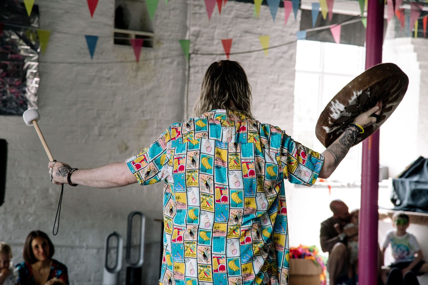 Person wearing colorful patterned shirt performing with props under festive bunting decorations.