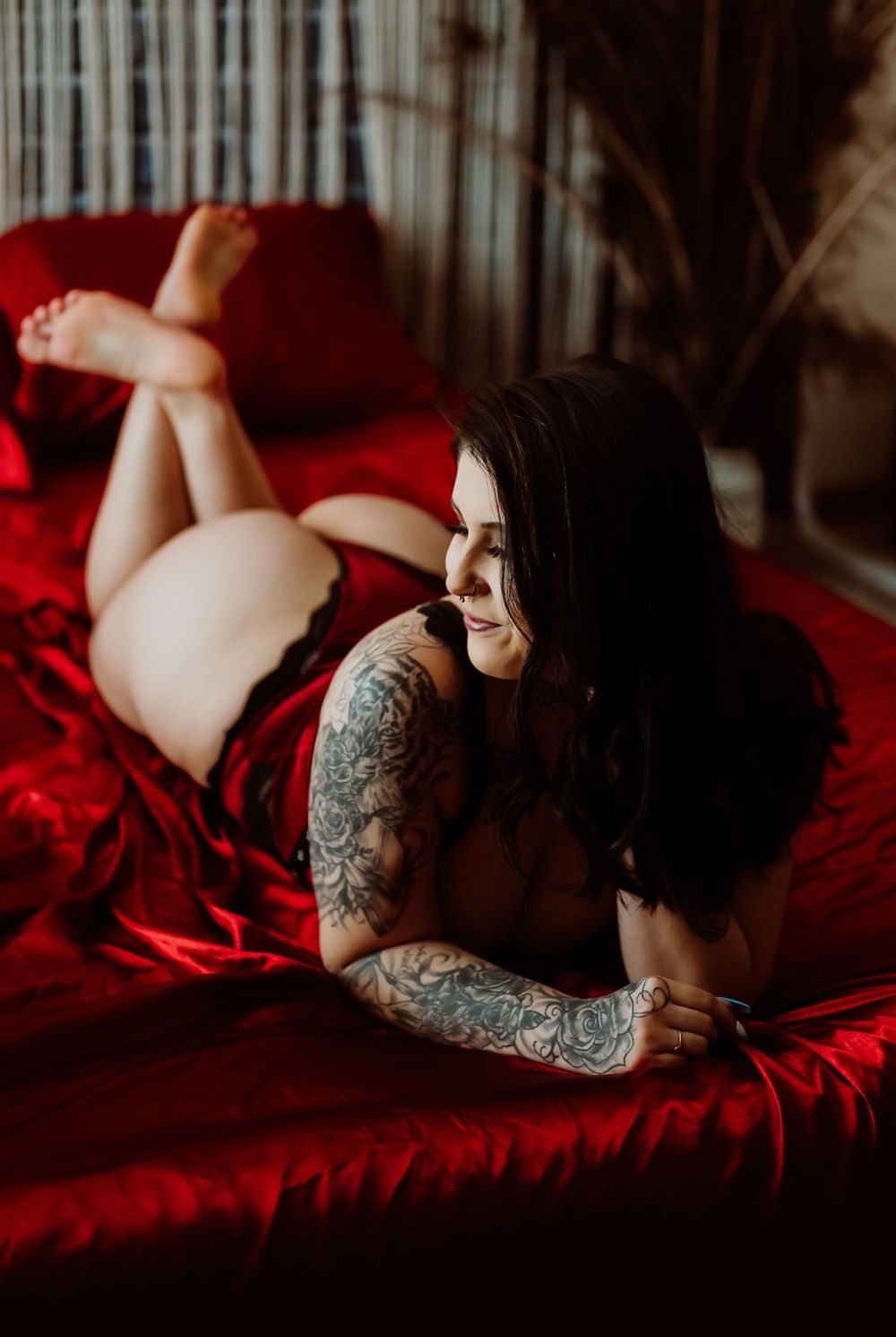 Artistic boudoir photography featuring dark tones, red bedding and elegant poses.