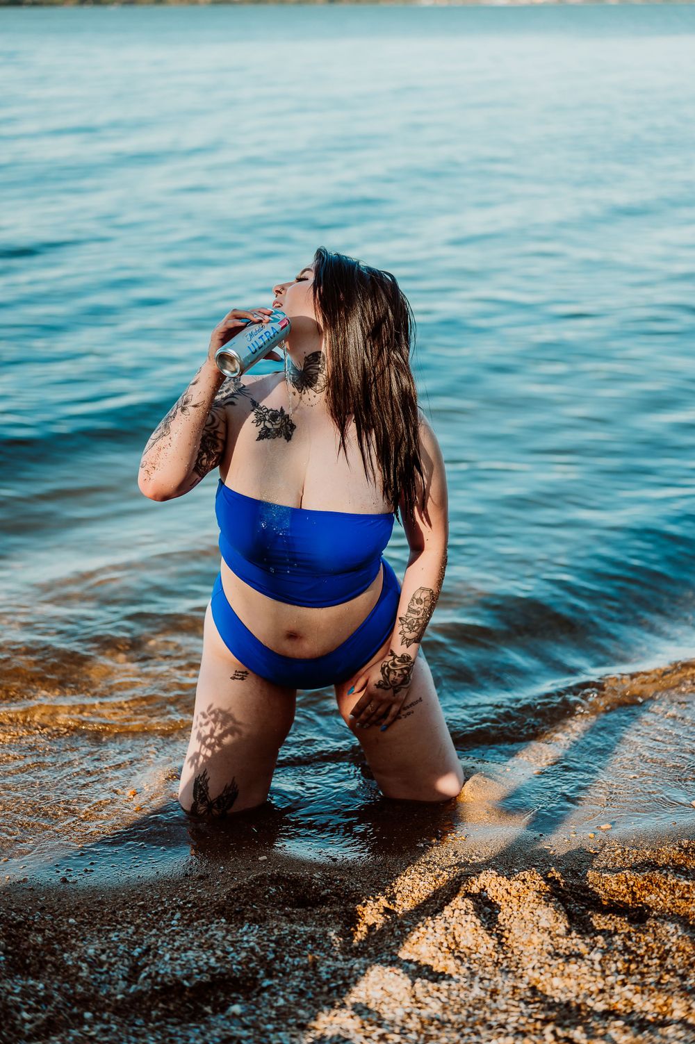 Model in blue swimwear poses at water's edge during golden hour.
