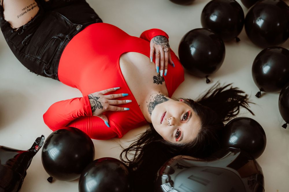 Artistic portrait session with black balloons and red outfit creating dramatic contrast.