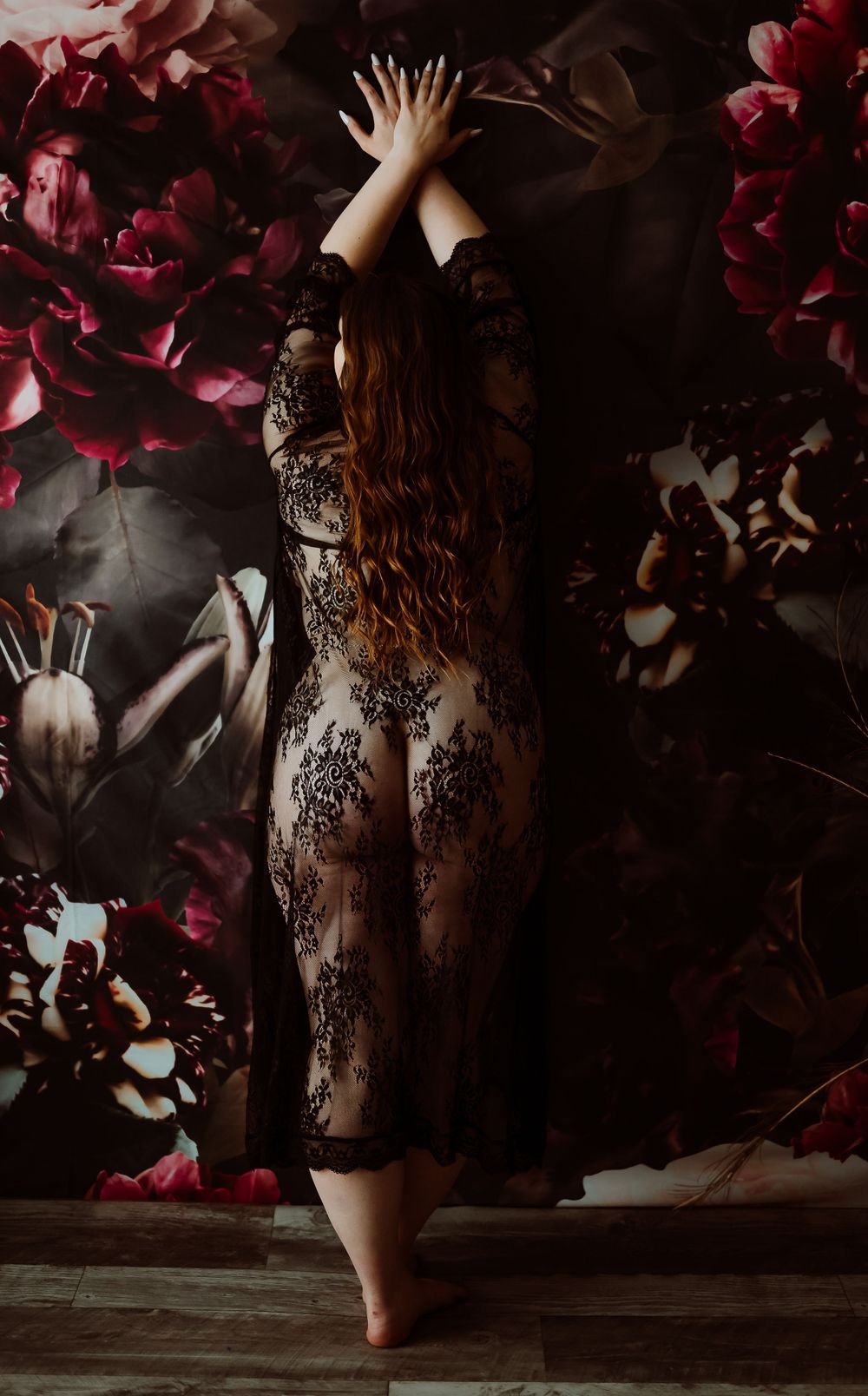 Artistic boudoir photoshoot with black lace lingerie against dark background with falling red rose petals.