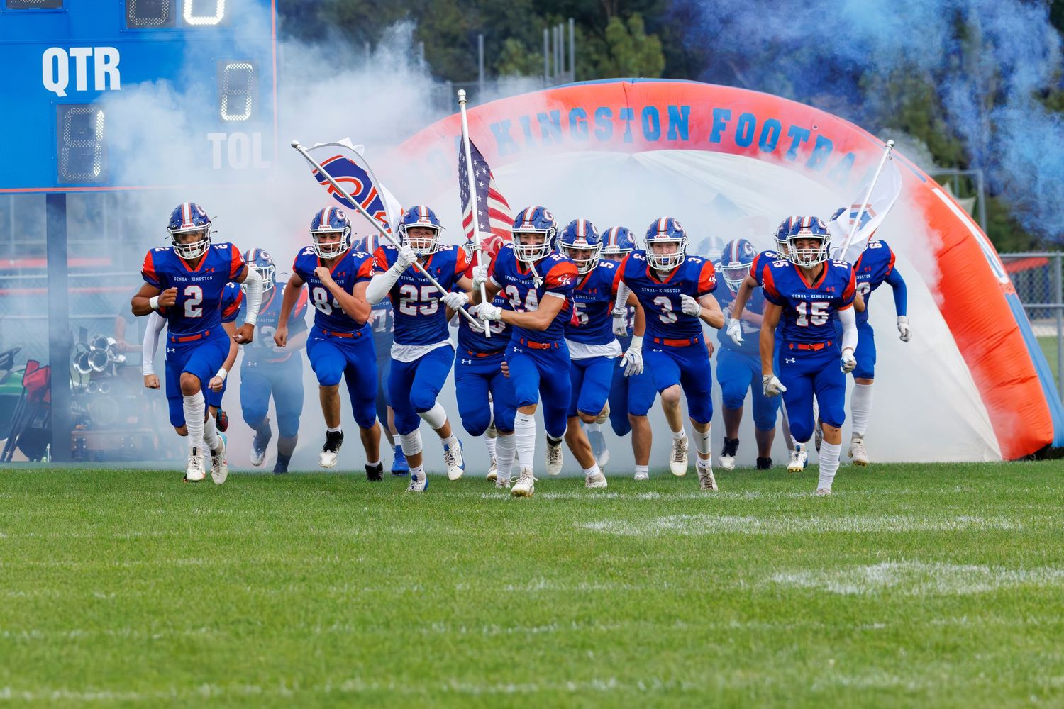 Football team running through smoke and banner entrance at stadium.