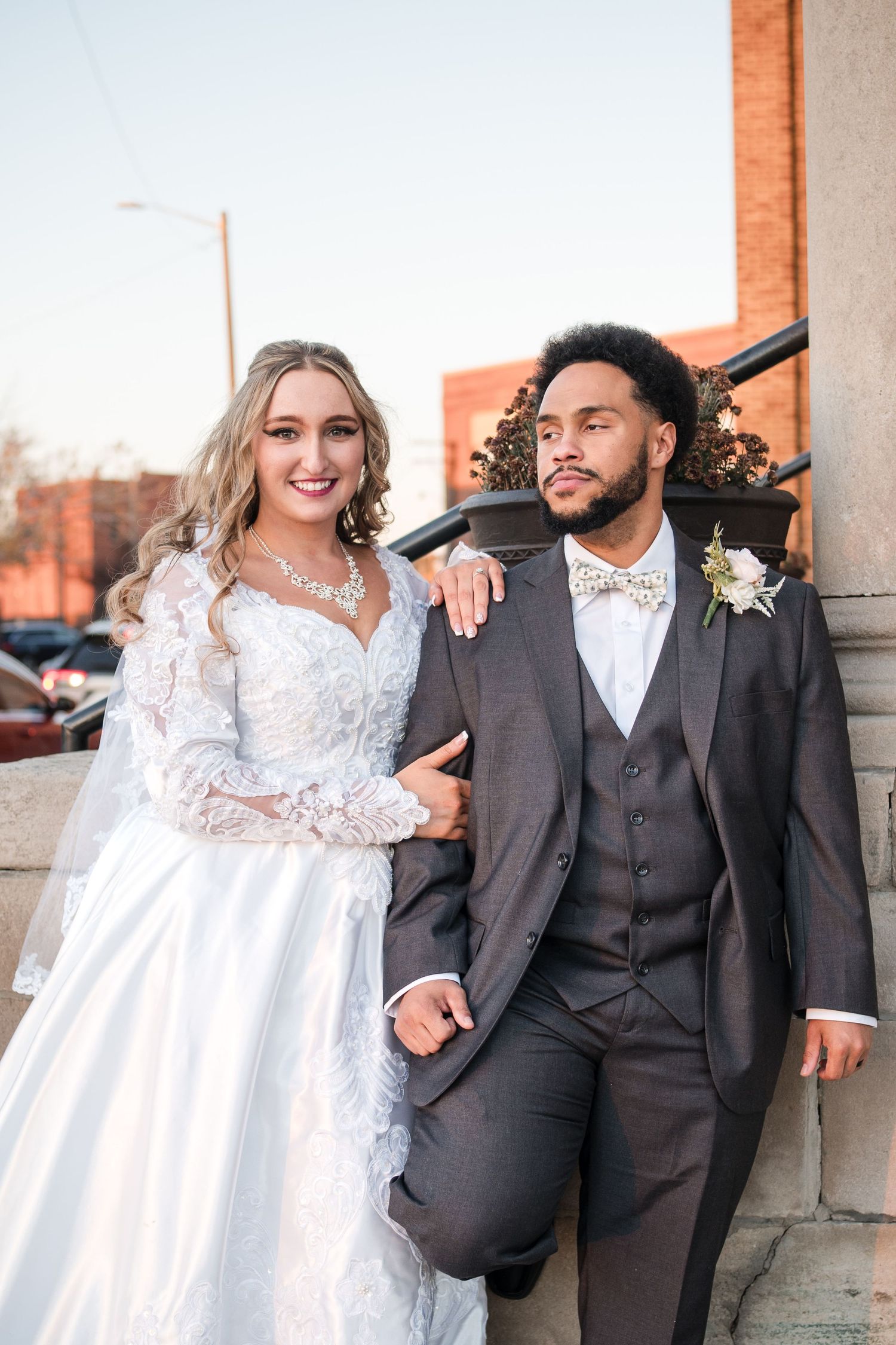 Romantic wedding portraits against a brick wall featuring elegant white dress and dark suit combinations.