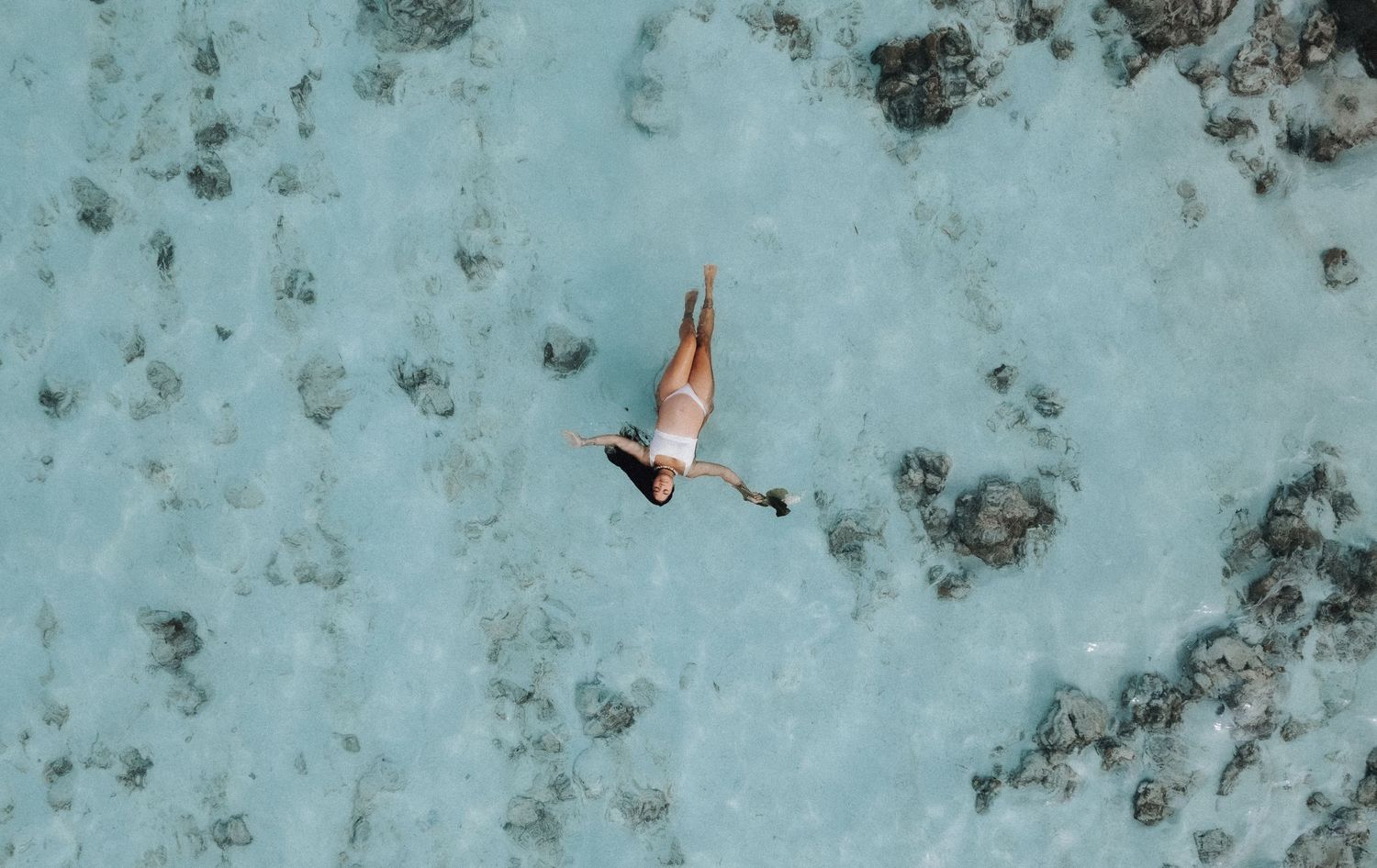 Aerial view of person swimming in crystal clear turquoise waters with coral reef patterns visible below.