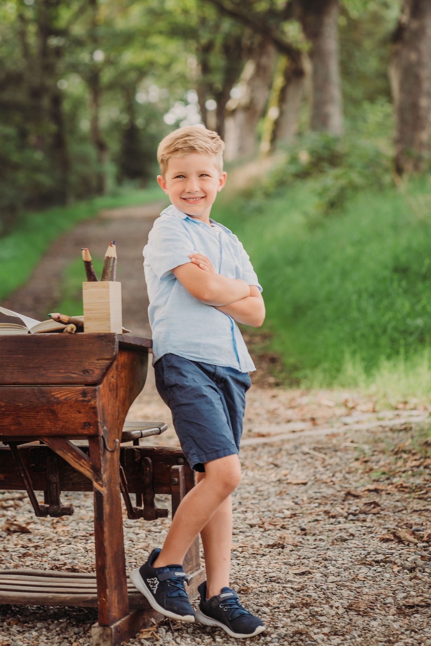 Student posing confidently next to vintage wooden desk on forest trail.