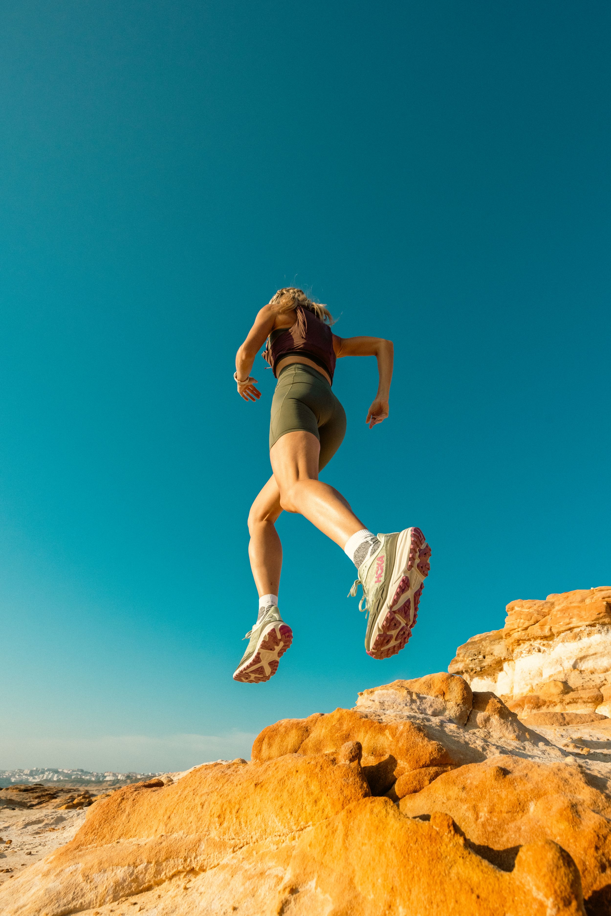 Athletic figure leaping over rocky terrain against bright blue sky in outdoor action shot.