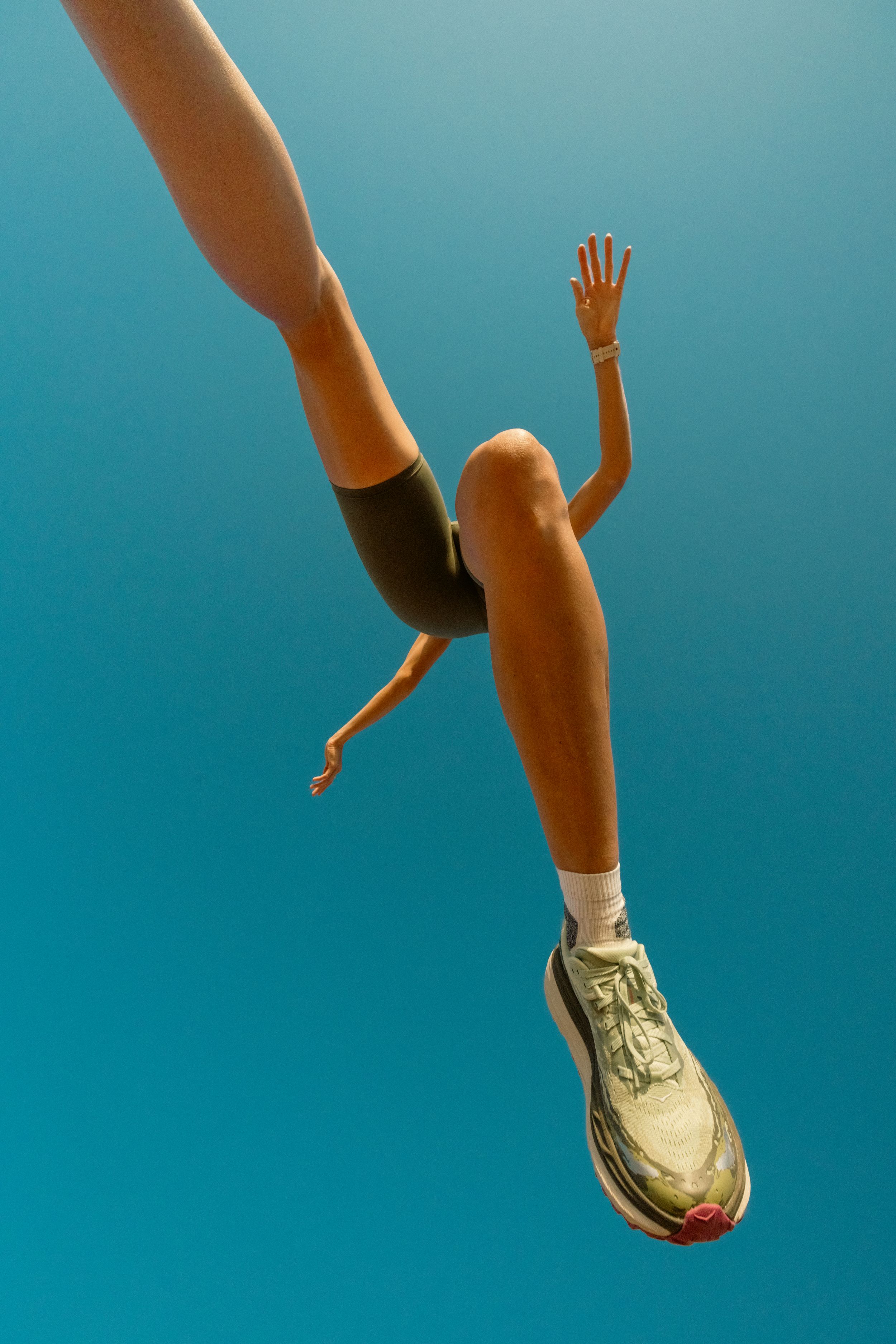 Dynamic shot of legs and sneakers suspended mid-air against bright blue background.
