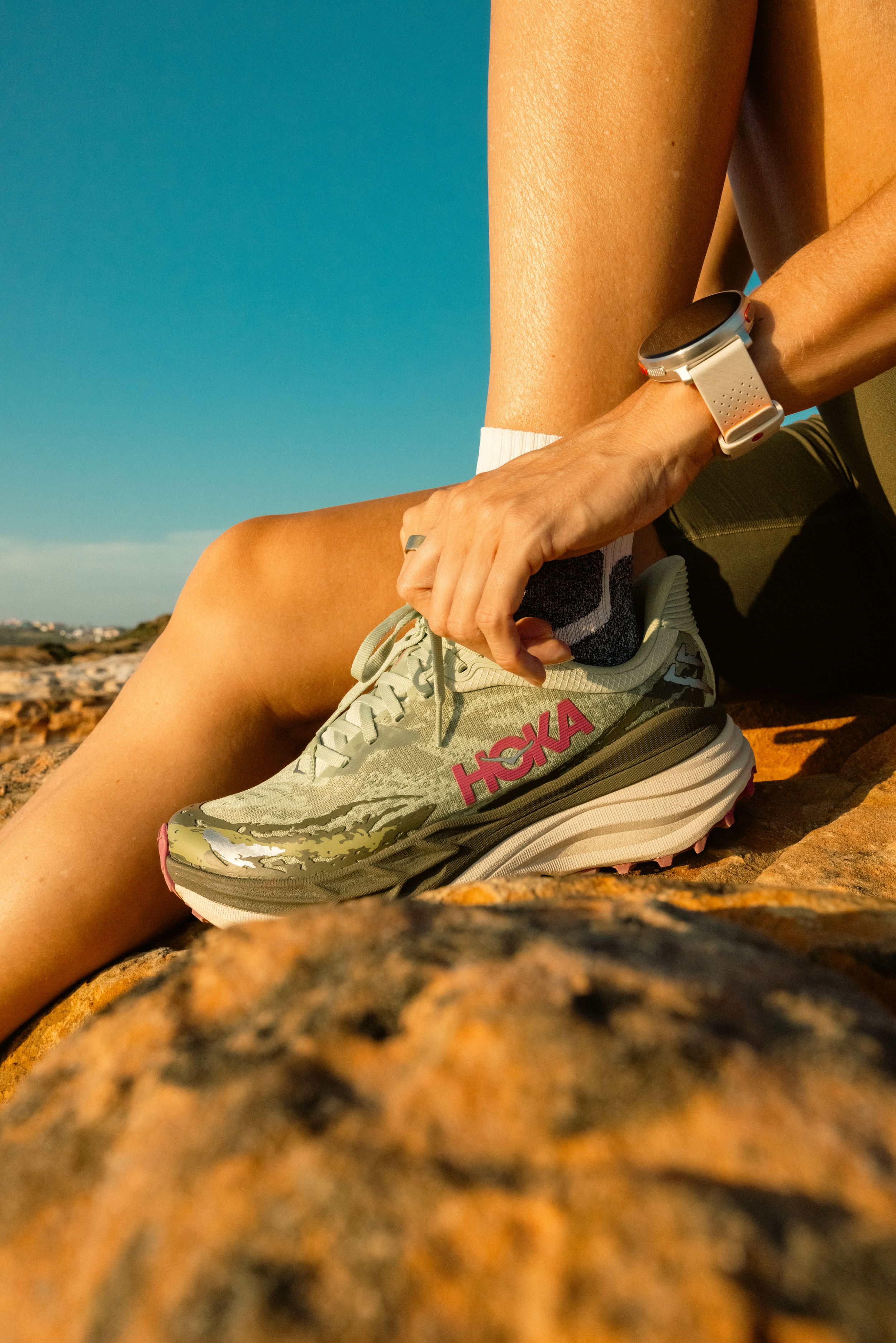 Detail shot of Hoka running shoe and leg resting on orange desert rock formation.