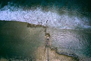 Aerial view of a wooden pier extending into ocean waves.
