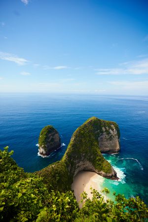 Stunning cliffside beach cove with turquoise waters and green vegetation in Nusa Penida, Indonesia.