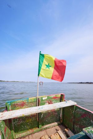 Senegalese flag flying on a boat over calm water.