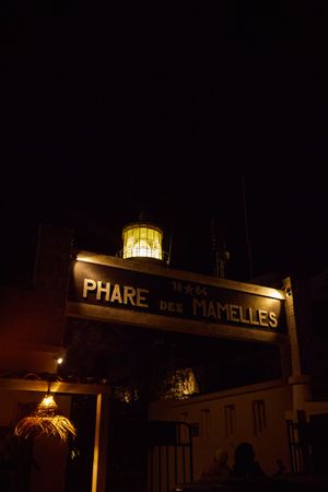 Illuminated lighthouse sign reading 'Phare des Mamelles' glowing against dark night sky.