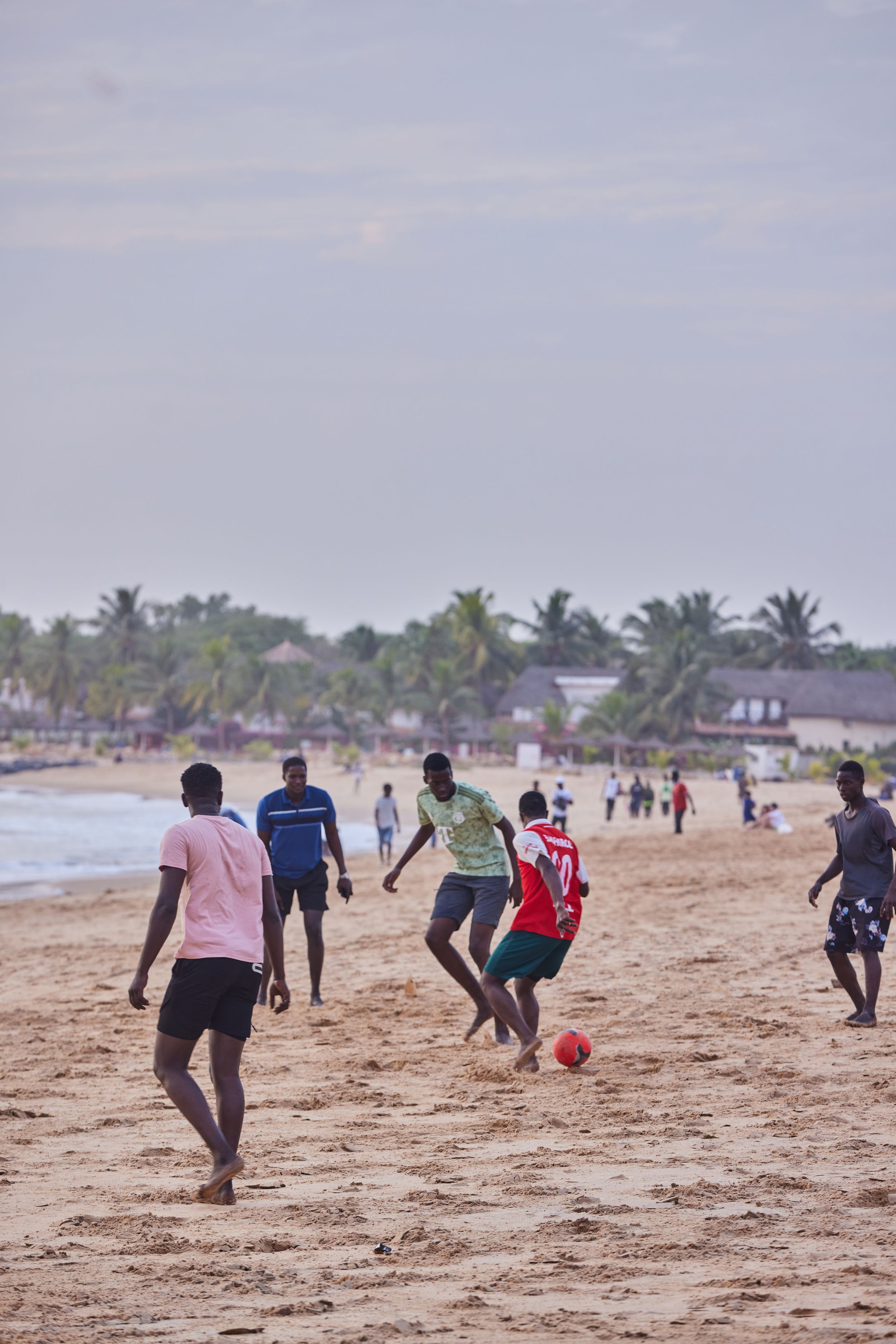 People playing soccer on sandy beach with palm trees in background.