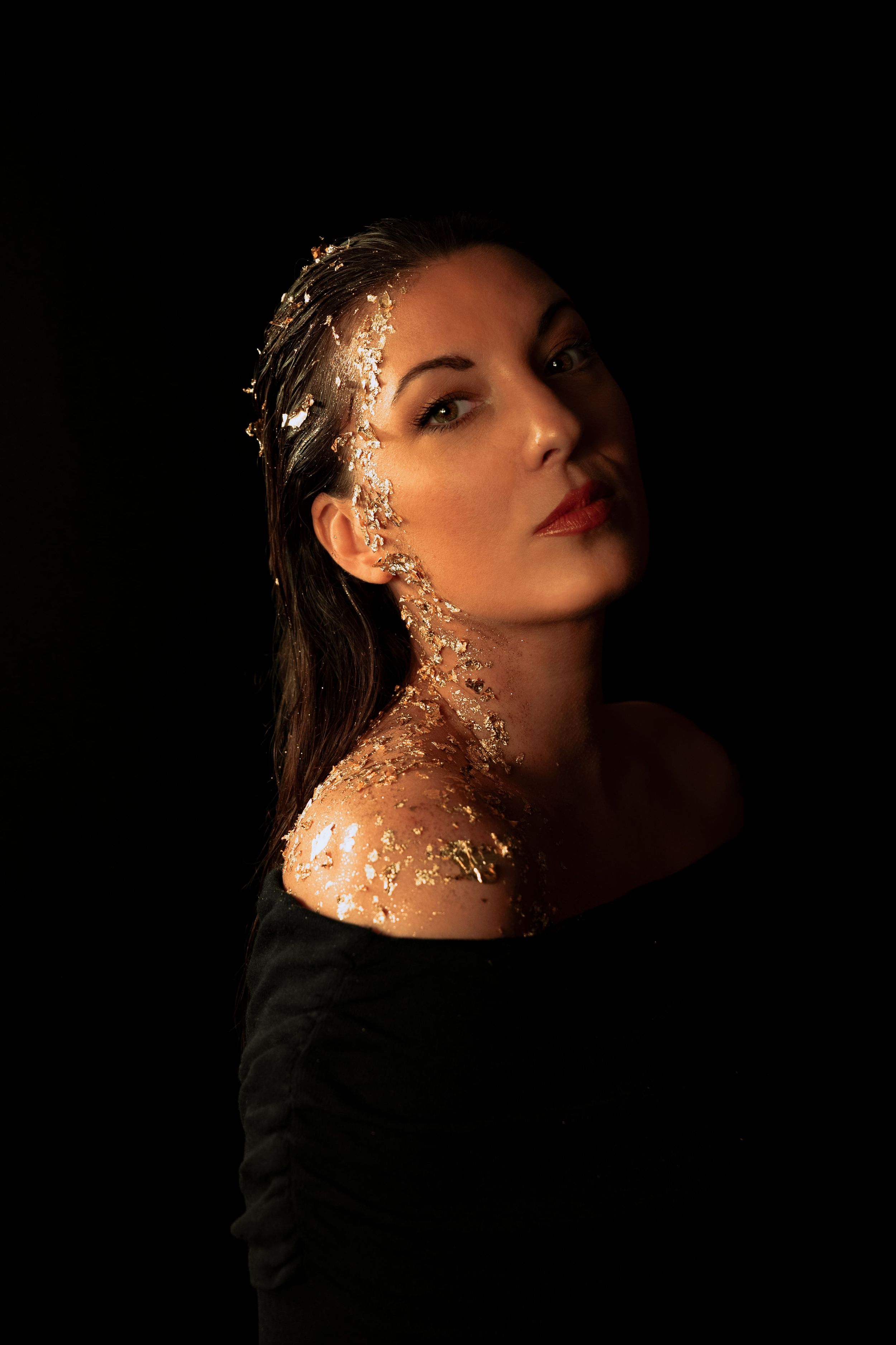 Artistic portrait with gold glitter details against dark background creating ethereal lighting effects.