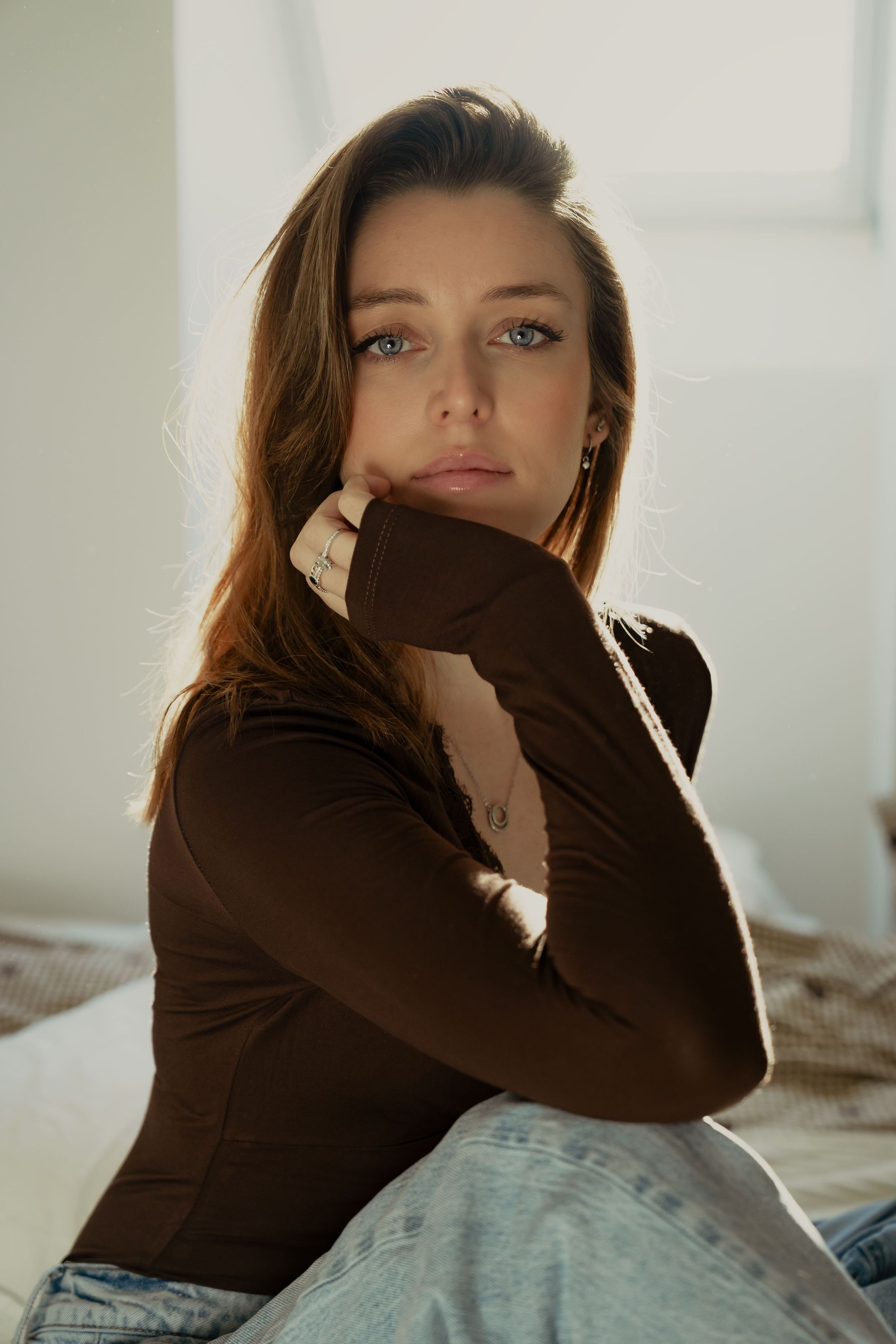 Lifestyle portraits of person in brown sweater lounging on bed in natural window light.