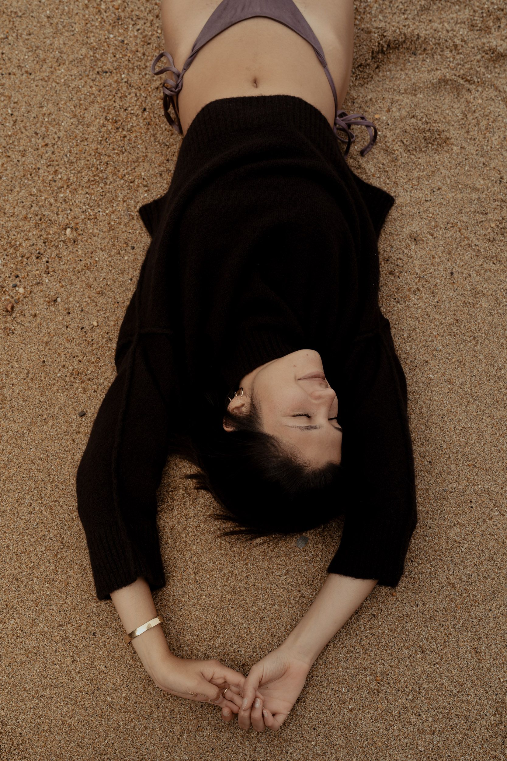Artistic overhead shot of person lying on sandy textured surface in dark clothing.