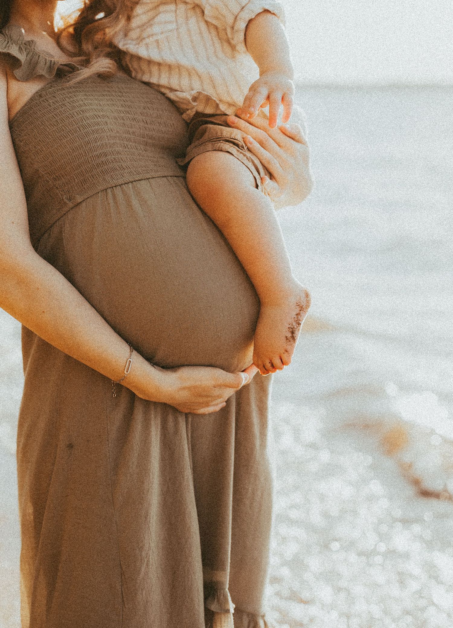 A couple stands together on a beach during a maternity photography session.