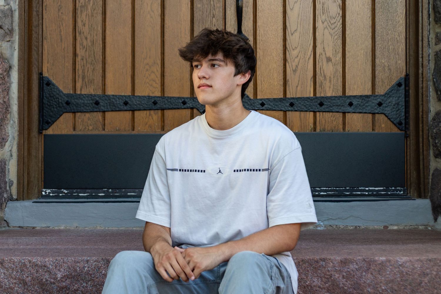 Young person in blue henley shirt sitting casually outdoors with a bright smile.